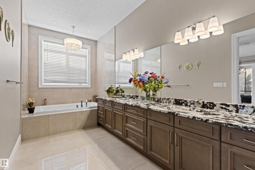 Full bath with a textured ceiling, double vanity, light tile patterned floors, a garden tub, and a chandelier - 2796 Wheaton Drive Nw, Edmonton, AB - Indoor Photo Showing Bathroom