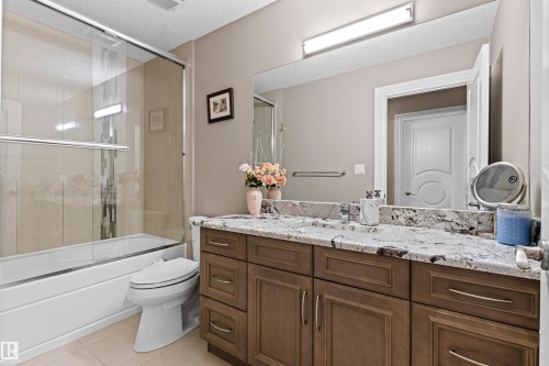 Bathroom featuring vanity, a textured ceiling, bath / shower combo with glass door, and light tile patterned floors - 2796 Wheaton Drive Nw, Edmonton, AB - Indoor Photo Showing Bathroom