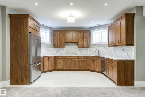 Kitchen featuring brown cabinets, appliances with stainless steel finishes, healthy amount of natural light, light stone counters, and recessed lighting - 2796 Wheaton Drive Nw, Edmonton, AB - Indoor Photo Showing Kitchen