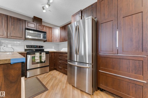 Kitchen featuring wood-finish cabinetry, stainless steel appliances, light wood-finish flooring, subway tile backsplash, and track lighting - #136 16035 132 St Nw, Edmonton, AB - Indoor Photo Showing Kitchen