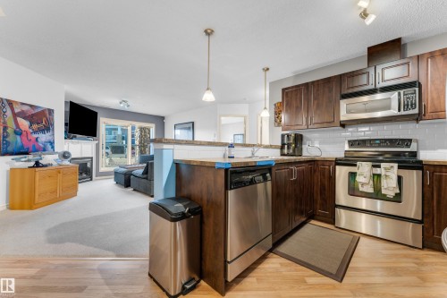 Kitchen featuring dark wood-finish cabinetry, stainless steel appliances, a white subway tile backsplash, and wood-finish flooring - #136 16035 132 St Nw, Edmonton, AB - Indoor Photo Showing Kitchen