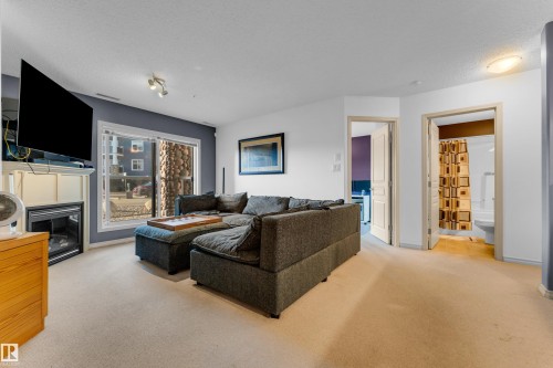 Living area featuring a fireplace with a white mantel, beige carpeting, and a sliding glass door - #136 16035 132 St Nw, Edmonton, AB - Indoor Photo Showing Living Room With Fireplace