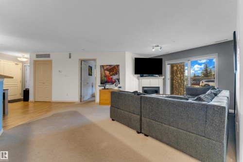 Living area featuring a white fireplace with mantle, sliding glass patio doors, and light wood-finish flooring transitioning to carpet - #136 16035 132 St Nw, Edmonton, AB - Indoor Photo Showing Living Room With Fireplace