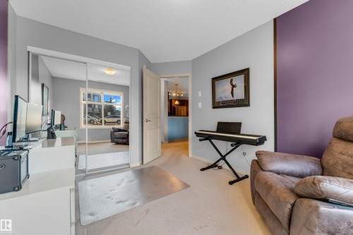 Room featuring light gray and purple accent walls, light-colored carpeting, a doorway with an interior light fixture visible, and a mirrored closet - #136 16035 132 St Nw, Edmonton, AB - Indoor