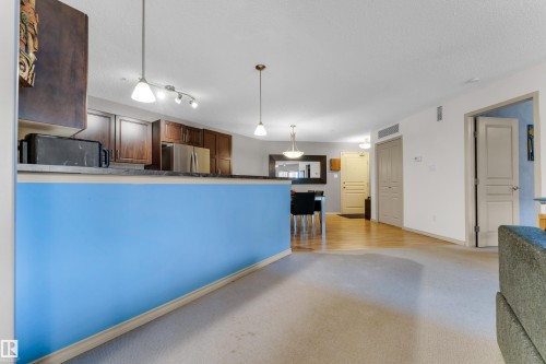 Open-concept living space featuring a carpeted area, hard surface flooring, and a kitchen with stainless steel appliances and wood cabinetry - #136 16035 132 St Nw, Edmonton, AB - Indoor