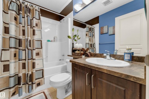 Bathroom featuring a built-in vanity with a brown countertop and wood-finish cabinetry, an oval undermount sink with a chrome faucet, a toilet, and a combined tub and shower unit with white surround - #136 16035 132 St Nw, Edmonton, AB - Indoor Photo Showing Bathroom