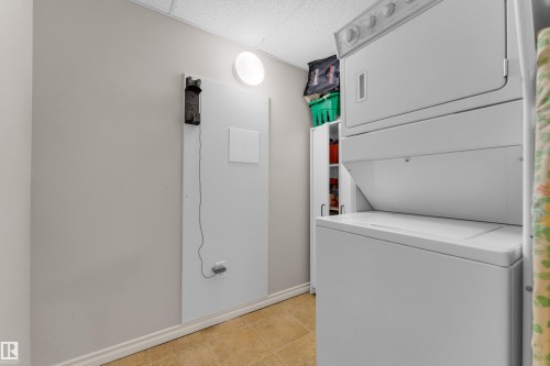 Dedicated utility area featuring a stacked washer and dryer, neutral wall paint, and tiled flooring - #136 16035 132 St Nw, Edmonton, AB - Indoor Photo Showing Laundry Room