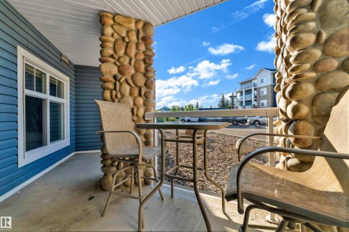 Covered patio space featuring a concrete floor, stone-clad support columns, and blue horizontal siding - #136 16035 132 St Nw, Edmonton, AB - Outdoor With Deck Patio Veranda