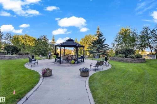 Spacious outdoor patio with a central gazebo, bordered by manicured lawns and retaining walls featuring established plantings - #136 16035 132 St Nw, Edmonton, AB - Outdoor With Deck Patio Veranda With Backyard