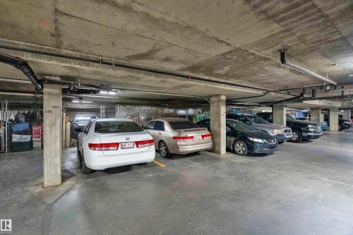 Underground parking garage featuring concrete pillars, exposed utility pipes, fluorescent lighting, and designated parking spaces - #136 16035 132 St Nw, Edmonton, AB - Indoor Photo Showing Garage