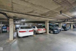 Underground parking garage featuring concrete pillars, exposed utility pipes, fluorescent lighting, and designated parking spaces - 