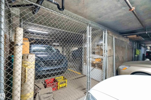 Secured parking area featuring chain-link fencing, concrete ceiling, overhead lighting, and exposed plumbing - #136 16035 132 St Nw, Edmonton, AB - Indoor