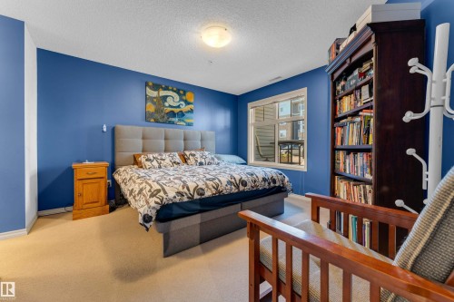 Carpeted bedroom featuring a large window, recessed lighting, and a built-in dark wood bookcase - #136 16035 132 St Nw, Edmonton, AB - Indoor Photo Showing Bedroom