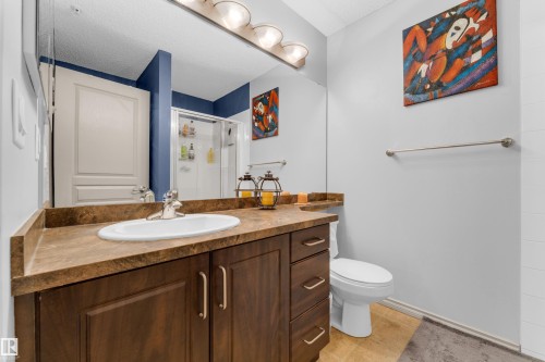Bathroom featuring a dark wood-finish vanity with an integrated sink, a light-colored countertop, a chrome faucet, and a large wall mirror - #136 16035 132 St Nw, Edmonton, AB - Indoor Photo Showing Bathroom