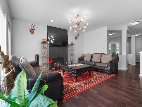 Expansive living area featuring rich wood-finish flooring and a contemporary sputnik-style chandelier - 1716 60 Street Sw, Edmonton, AB - Indoor Photo Showing Living Room With Fireplace