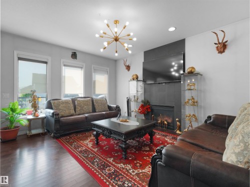 Living area featuring dark wood-finish flooring, light gray walls, and a contemporary sputnik chandelier - 1716 60 Street Sw, Edmonton, AB - Indoor Photo Showing Living Room With Fireplace