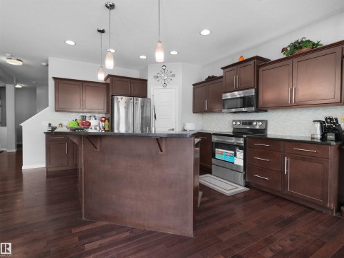 Spacious kitchen featuring dark wood-finish cabinetry, stainless steel appliances, a center island with countertop seating, recessed lighting, and wood-finish flooring - 1716 60 Street Sw, Edmonton, AB - Indoor Photo Showing Kitchen With Stainless Steel Kitchen With Upgraded Kitchen