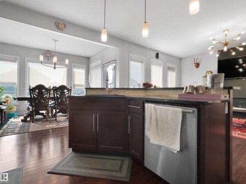 Open-concept kitchen featuring dark wood-finish cabinetry, a stainless steel dishwasher, and a dark stone countertop - 1716 60 Street Sw, Edmonton, AB - Indoor Photo Showing Kitchen