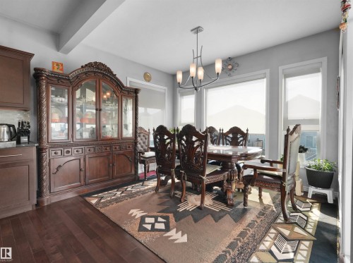 Spacious dining area featuring dark wood-finish flooring, a contemporary chandelier, multiple windows with roller shades, and light gray wall paint - 1716 60 Street Sw, Edmonton, AB - Indoor Photo Showing Dining Room