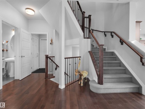 Expansive foyer featuring rich wood-finish flooring and a carpeted staircase with dark wood handrails and wrought iron balusters - 1716 60 Street Sw, Edmonton, AB - Indoor Photo Showing Other Room