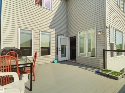 Spacious outdoor deck featuring composite decking, a clear railing system, multiple windows, and exterior siding - 