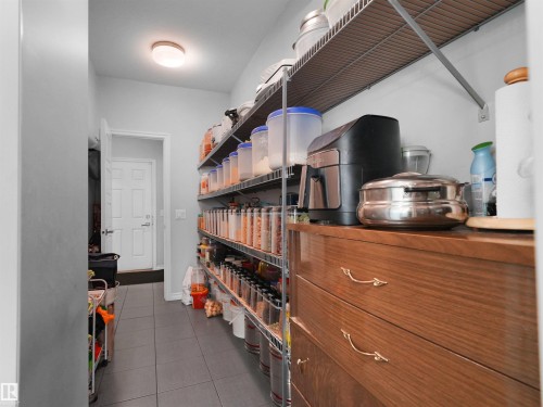 Spacious pantry featuring extensive wire shelving, a built-in wood-finish cabinet with gold-tone hardware, and contemporary gray tile flooring - 1716 60 Street Sw, Edmonton, AB - Indoor