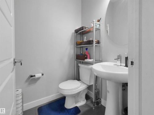 Pedestal sink with chrome faucet, circular wall-mounted mirror, and white toilet - 1716 60 Street Sw, Edmonton, AB - Indoor Photo Showing Bathroom