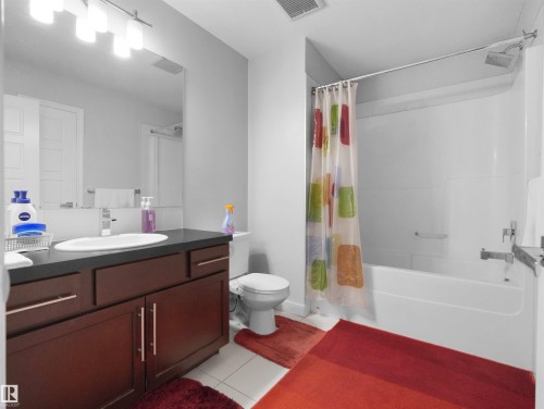 Bathroom featuring a dark wood-finish vanity with a single basin sink, a large wall-mounted mirror, and a full bathtub with an overhead shower - 1716 60 Street Sw, Edmonton, AB - Indoor Photo Showing Bathroom