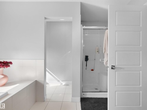 Bathroom featuring a white tile half-wall, a walk-in shower with a glass enclosure, a five-panel interior door, and light gray wall paint - 1716 60 Street Sw, Edmonton, AB - Indoor