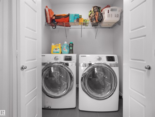 Dedicated laundry space featuring a side-by-side washer and dryer, tile flooring, and integrated wire shelving for storage - 1716 60 Street Sw, Edmonton, AB - Indoor Photo Showing Laundry Room