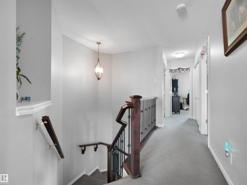 Upper-level hallway featuring light gray walls, plush carpet flooring, a dark wood newel post with wrought iron spindles, a matching handrail, and a contemporary pendant light fixture - 1716 60 Street Sw, Edmonton, AB - Indoor Photo Showing Other Room
