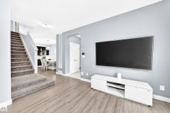 Spacious living area featuring wood-finish flooring, light gray wall tones, and a carpeted staircase with white risers - 