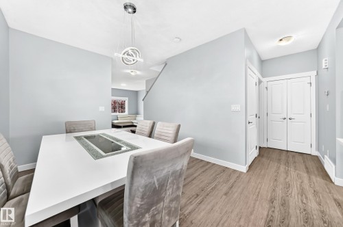 Dining area featuring a contemporary chandelier, light wood-finish flooring, white baseboards, and a white interior door - 17508 58 Street Nw, Edmonton, AB - Indoor
