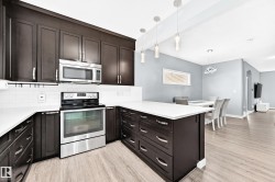 Modern kitchen featuring dark wood-finish cabinetry, stainless steel appliances including a built-in microwave and range, white subway tile backsplash, and light-toned wood-finish flooring - 