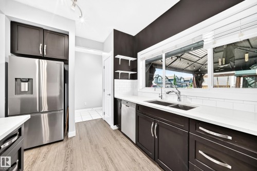 Modern kitchen featuring wood-finish flooring, dark cabinetry, and light countertops - 17508 58 Street Nw, Edmonton, AB - Indoor Photo Showing Kitchen With Double Sink