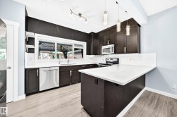 Modern kitchen featuring dark wood-finish cabinetry, stainless steel appliances, a white subway tile backsplash, and light wood-finish flooring - 