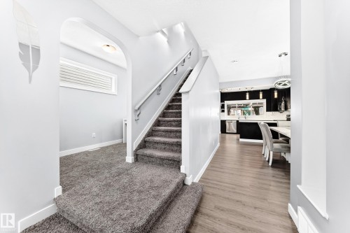 Carpeted staircase with white railings and risers leading to an upper level, complemented by wood-finish flooring extending into a kitchen area - 17508 58 Street Nw, Edmonton, AB - Indoor Photo Showing Other Room
