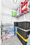 Recessed ceiling lighting illuminates a storage area featuring white wire shelving units and grey carpet flooring - 