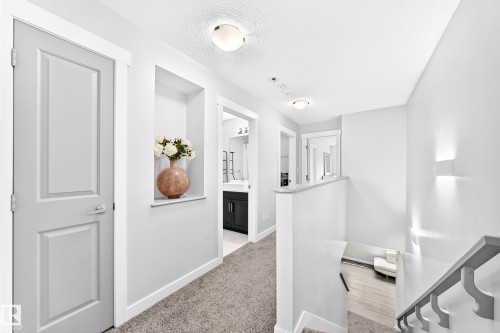 Carpeted hallway with a built-in wall niche, multiple recessed lighting fixtures, and a white balustrade leading to a lower level with wood-finish flooring - 17508 58 Street Nw, Edmonton, AB - Indoor Photo Showing Other Room