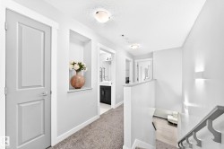 Carpeted hallway with a built-in wall niche, multiple recessed lighting fixtures, and a white balustrade leading to a lower level with wood-finish flooring - 