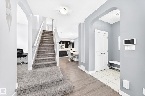 Carpeted staircase with white railings, flanked by an arched entryway with wood-finish flooring and a tiled entryway with a white door - 17508 58 Street Nw, Edmonton, AB - Indoor Photo Showing Other Room