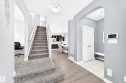 Carpeted staircase with white railings, flanked by an arched entryway with wood-finish flooring and a tiled entryway with a white door - 