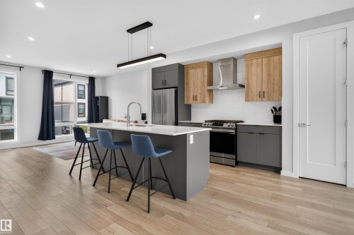 Contemporary kitchen featuring an oversized island with countertop seating, stainless steel appliances, and a tile backsplash - #84 1304 Rutherford Rd Sw, Edmonton, AB - Indoor Photo Showing Kitchen With Stainless Steel Kitchen With Upgraded Kitchen