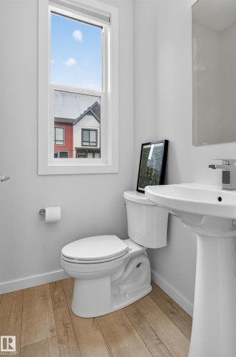 Powder room featuring a single-pane window, wood-finish flooring, white pedestal sink, and modern chrome faucet - #84 1304 Rutherford Rd Sw, Edmonton, AB - Indoor Photo Showing Bathroom