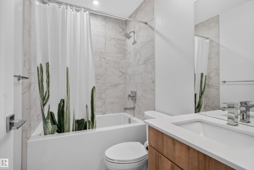 Contemporary bathroom featuring a spacious white tub, marble-finish wall tiling, a wood-finish vanity with an integrated sink, and chrome fixtures - #84 1304 Rutherford Rd Sw, Edmonton, AB - Indoor Photo Showing Bathroom