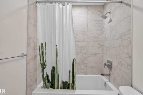 Bathtub shower combination featuring white subway tile with a marble-effect, a rain shower head, and chrome fixtures - #84 1304 Rutherford Rd Sw, Edmonton, AB - Indoor Photo Showing Bathroom