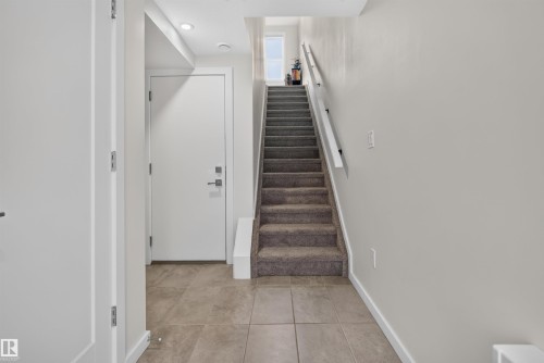 Entryway featuring light-toned tile flooring, a carpeted staircase with white handrails, flush-mount ceiling lighting, and a white interior door with contemporary hardware - #84 1304 Rutherford Rd Sw, Edmonton, AB - Indoor Photo Showing Other Room