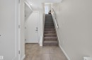 Entryway featuring light-toned tile flooring, a carpeted staircase with white handrails, flush-mount ceiling lighting, and a white interior door with contemporary hardware - #84 1304 Rutherford Rd Sw, Edmonton, AB  - Indoor Photo Showing Other Room 