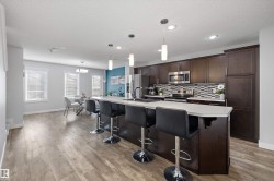 Kitchen featuring a large island with seating, dark wood cabinetry, stainless steel appliances, a mosaic tile backsplash, and light-toned countertops - 