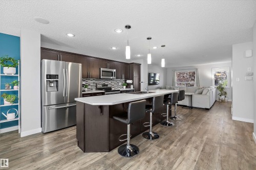 Contemporary kitchen featuring dark wood cabinetry, stainless steel appliances, a mosaic tile backsplash, and a large island with white countertops - 12305 173A Avenue Nw, Edmonton, AB - Indoor Photo Showing Kitchen With Upgraded Kitchen